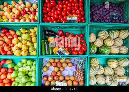 A diverse and colorful array of fresh fruits and vegetables, including apples, pears, tomatoes, and melons, showcased in green crates at a Vannes mark Stock Photo