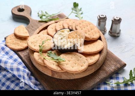 Tasty crackers with bowl of sauce and arugula on light blue background Stock Photo