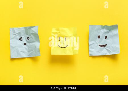 Crumpled sticky notes with drawings of different emotion faces on yellow background Stock Photo