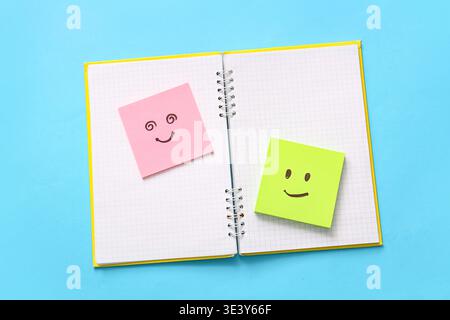 Notebook and sticky papers with drawn happy faces on blue background Stock Photo
