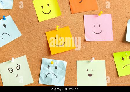 Sticky notes with drawings of different emotion faces on cork board as background Stock Photo