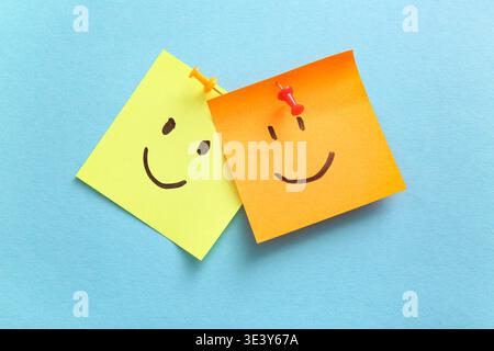 Pinned sticky papers with drawn happy faces on blue background Stock Photo