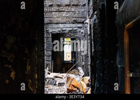 Charred wooden interior of a home after a devastating fire, revealing stark destruction and ruined structure. A glimpse of light through a distant win Stock Photo