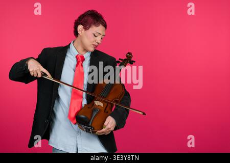 Person holding violin with bow posing on pink background Stock Photo