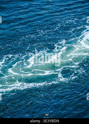 Whirling white aquatic foam creates a detailed bubbling texture on the dark sea water caused by boat motion in a tropical environment. Stock Photo