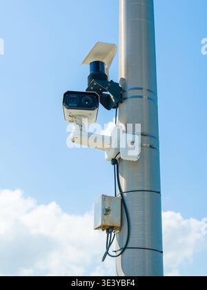 A pair of modern CCTV surveillance cameras is installed on a pole with an electrical box. Professional security equipment for urban safety. Stock Photo