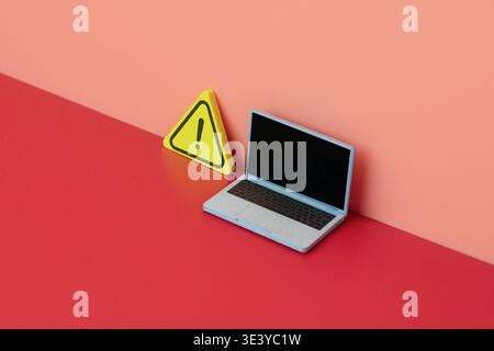 A laptop next to a yellow wooden warning sign. Computer security, technical errors, online threats, and system alerts concept. Copy space for text. Stock Photo