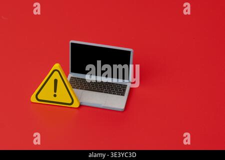 A laptop next to a yellow wooden warning sign. Computer security, technical errors, online threats, and system alerts concept. Copy space for text. Stock Photo