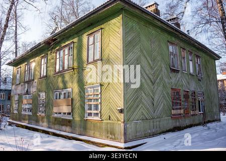 Weathered green abandoned house, windows boarded up, stands in a snowy winter landscape. Dilapidated facade reflects a forgotten past, evoking feeling Stock Photo