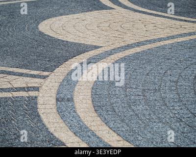 Decorative curved pavement mosaic made of blue and beige stone tiles forming concentric waves and geometric patterns on an urban plaza surface, emphas Stock Photo