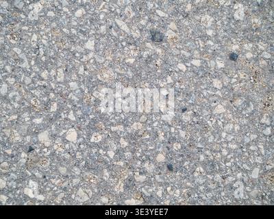 Grey asphalt with scattered pebbles and small stones. Surface shows wear from weather and use. Texture suggests road or pavement close-up. Ideal for c Stock Photo