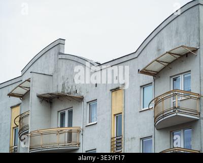 Curved concrete building with gold railings. Windows and balconies line the structure. Overcast sky frames the architectural design. Modern urban dwel Stock Photo