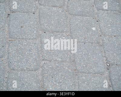 Gray stone paving stones form a textured grid. Tiny pebbles and dust dot the surface. Natural wear adds character to the stones. Ideal for urban or ga Stock Photo