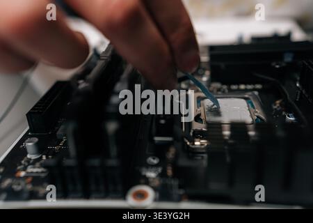 Close-up hands of unrecognizable technician applying thermal paste on computer processor, spreading precise layer for efficient cooling and improved Stock Photo