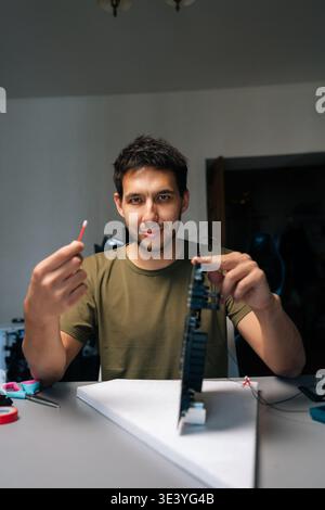 Vertical portrait of skilled computer service technician repairing computer part while holding cotton swab and looking at camera, sitting at desk in Stock Photo