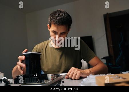 Portrait of computer technician male installing CPU cooler onto motherboard, performing maintenance and repair work on desktop computer in dark Stock Photo