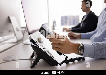 Closeup hand male operator take landline telephone receiver on workplace Stock Photo