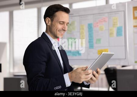 Smiling mid aged businessman using electronic pad in work office Stock Photo