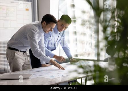 Two multiethnic businessmen leaning on office desk reviewing statistical information Stock Photo