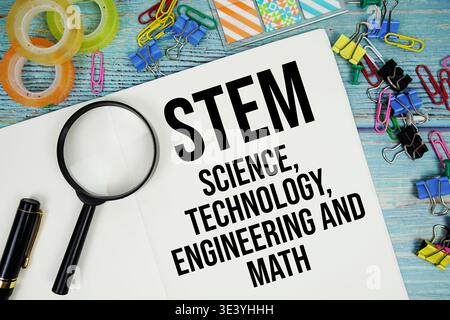 STEM Science, Technology, Engineering and Math text on a paper surrounded by office supplies and magnifying glass on a blue wooden surface Stock Photo