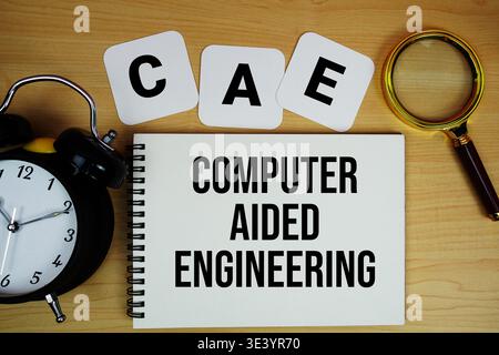 CAE Computer Aided Engineering text written on notepad with magnifying glass and alarm clock on wooden background Stock Photo