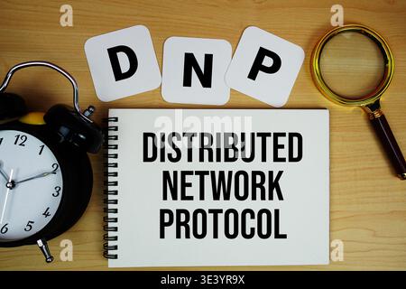 DNP Distributed Network Protocol text written on notepad with magnifying glass and alarm clock on wooden background Stock Photo