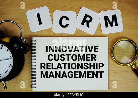 ICRM Innovative Customer Relationship Management text written on notepad with magnifying glass and alarm clock on wooden background Stock Photo