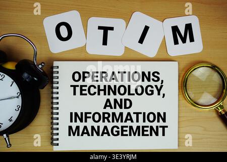 OTIM Operations, Technology, and Information Management text written on notepad with magnifying glass and alarm clock on wooden background Stock Photo