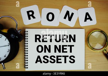 RONA Return On Net Assets text written on notepad with magnifying glass and alarm clock on wooden background Stock Photo