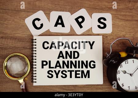 CAPS Capacity And Planning System text written on notepad with magnifying glass and alarm clock on wooden background Stock Photo