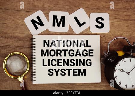 NMLS National Mortgage Licensing System text written on notepad with magnifying glass and alarm clock on wooden background Stock Photo