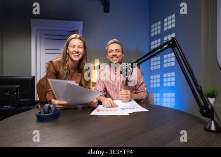 Portrait of podcasters reviewing printed analytics reports in recording studio Stock Photo