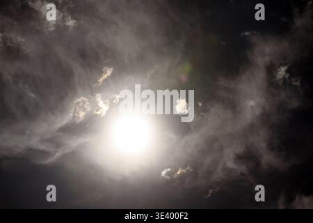 Bright sun shines through dark storm clouds. Light rays pierce through dense fog. Sky scene shows dramatic weather. Perfect for themes like hope, resi Stock Photo