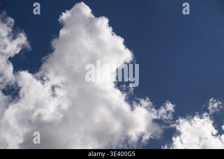 Large, fluffy white cloud towers against deep blue sky. Cloud forms dynamic shape, evoking calm or wonder. Great for backgrounds, travel, weather, or Stock Photo