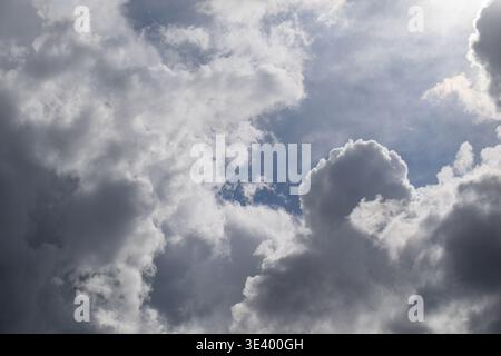 Dramatic clouds fill the sky with soft sunlight breaking through. Textures range from fluffy white to dark gray. Mood feels intense, with light and sh Stock Photo