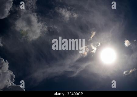 Sun glows brightly through wispy clouds against deep blue sky. Dramatic lighting creates soft shadows and highlights. Perfect for themes of hope, natu Stock Photo