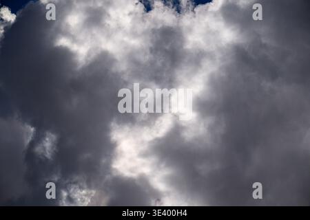 Dramatic sky filled with dense, textured storm clouds. Light breaks through cloud layers, creating contrast. Dark grey tones suggest an approaching st Stock Photo