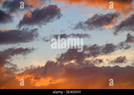 Dramatic sunset sky with clouds lit in fiery orange and soft blue. Dark cloud formations contrast warm tones beautifully. Ideal for backgrounds needin Stock Photo