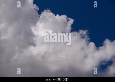 Large, fluffy white clouds float against deep blue sky. Clouds have soft, textured edges with gentle shadows. Scene feels calm and serene, perfect for Stock Photo