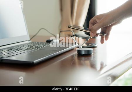 Charging mobile phone battery with wireless charging device in the table. Smartphone charging on a charging pad. Stock Photo
