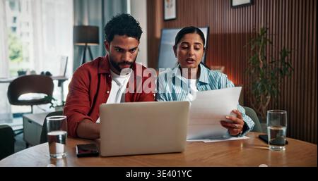 Couple, laptop and checking with documents for finance, investment or audit together in home. Man, woman or invoice with computer or paperwork for Stock Photo