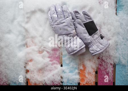 Warm gloves resting on colorful wooden surface in snow Stock Photo
