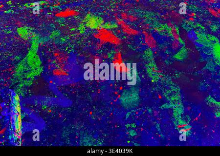Close-up of fiery red, deep blue neon paint splashes glowing under blacklight, forming vivid patterns for abstract art and graphic design. Stock Photo