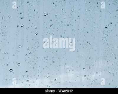 High-resolution close-up of raindrops on glass creating a soft blue abstract background. Perfect for weather, freshness, calm mood, and modern design Stock Photo