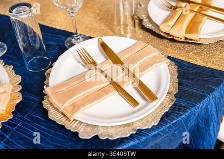 Elegant table setting with gold cutlery and folded napkin on white plate. Stock Photo