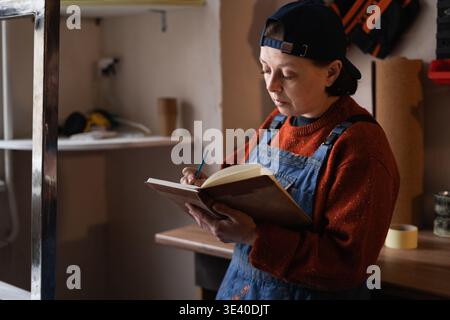 Female repairman writing notes while working in workshop. DIY concept. Stock Photo