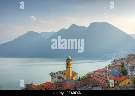 Scenic view of Colonno village on Lake Como. Historic church tower and red roofs with misty mountains in the background, Lombardy region, Italy Stock Photo