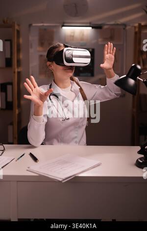 woman doctor using virtual reality goggles for medical purposes working during night shift at hospital. VR medicine concept. copy space Stock Photo