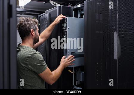 An IT technician works inside a data center rack, installing and maintaining server hardware and cables to ensure network performance, uptime, and infrastructure reliability for enterprise systems. || Model released Stock Photo