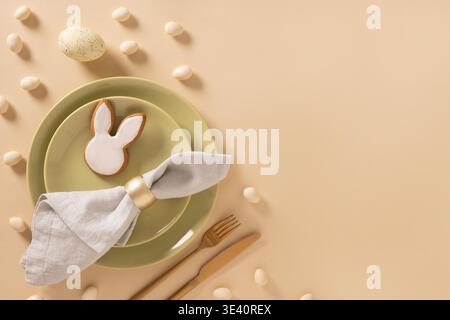 Easter table setting background with white plate, cookies , eggs and bunny on beige background. View from above. Space for greeting text. Stock Photo